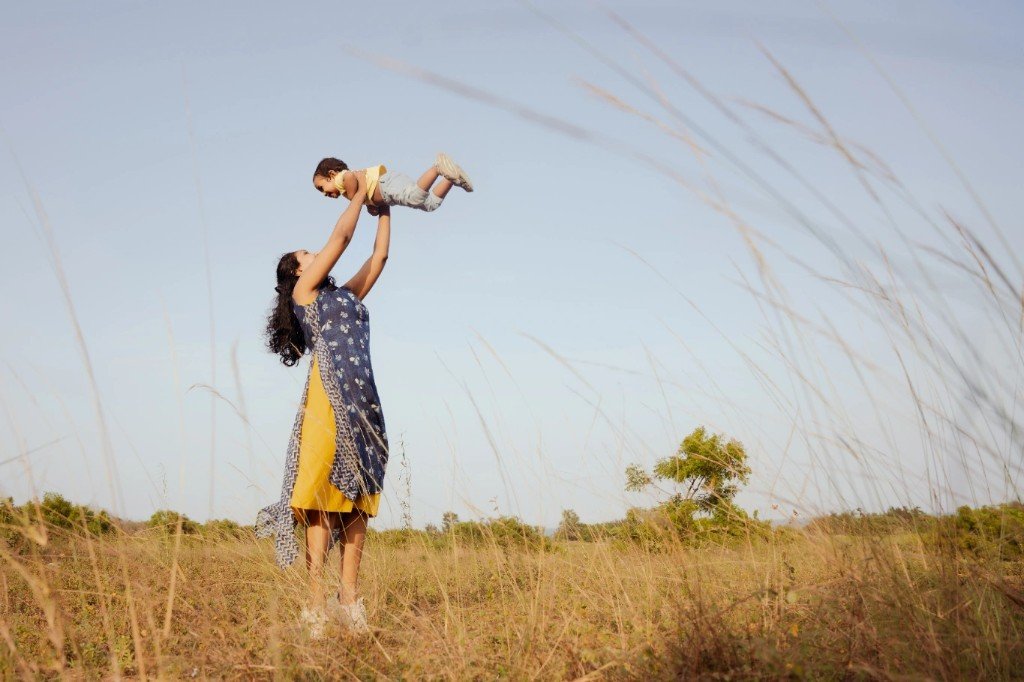 A mother lifting her child in a sunny field